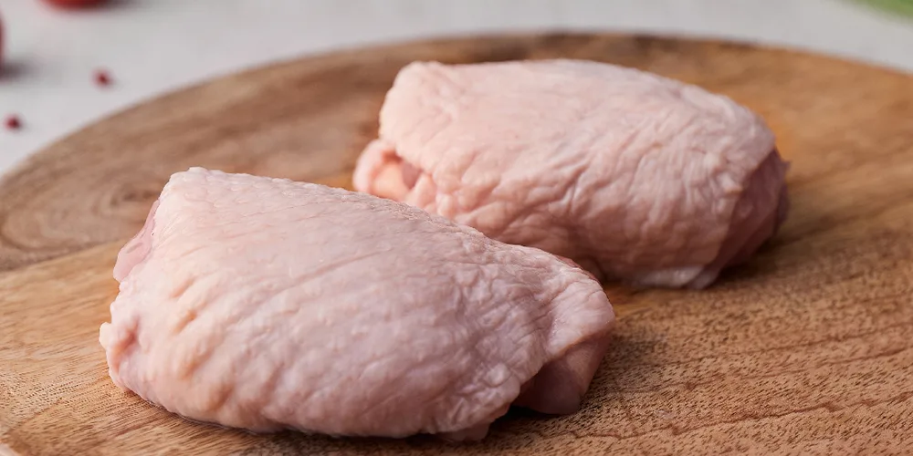 Two raw skin-on chicken thighs on a wooden board